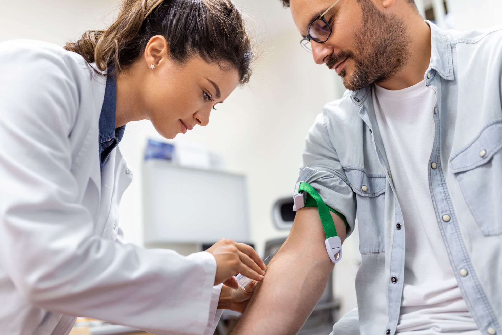 Friendly hospital phlebotomist collecting blood sample from patient in lab. Preparation for blood test by female doctor medical uniform on the table in white bright room;